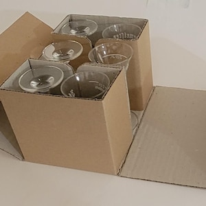May include: An open cardboard box containing several clear glass stemware glasses. The glasses are nestled in individual compartments within the box, which is made of corrugated cardboard. The box is partially open, revealing the contents.