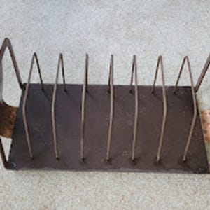 May include: A rectangular metal rack with a dark brown base and a series of vertical wire dividers. The structure features copper-toned side panels with curved handles at each end, providing a structured storage solution for organizing items.