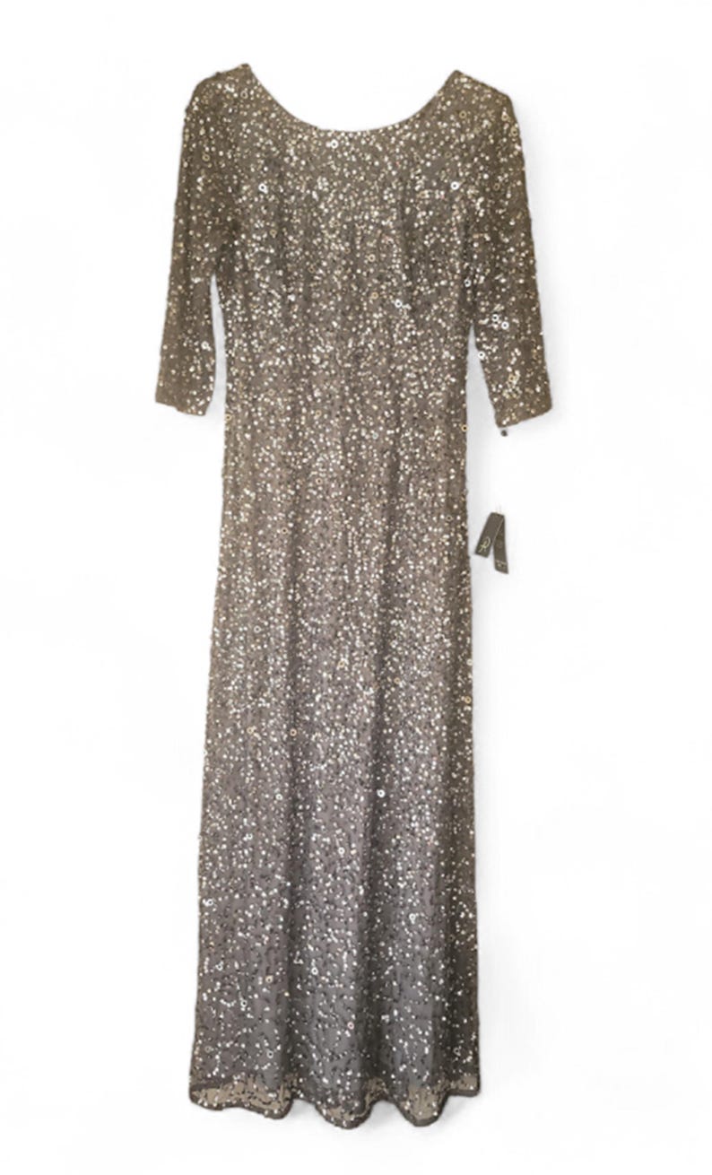 Puede incluir: Vestido largo con mangas tres cuartos, cubierto de lentejuelas brillantes. El vestido tiene un escote redondo y una etiqueta. El vestido es de color neutro, posiblemente plateado o gris.