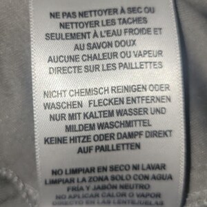 Puede incluir: Etiqueta de tela blanca con instrucciones de cuidado en ingl&eacute;s, franc&eacute;s, alem&aacute;n, espa&ntilde;ol y checo. La etiqueta desaconseja la limpieza en seco y el lavado, y recomienda limpiar las manchas con agua fr&iacute;a.