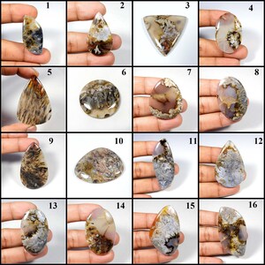 May include: A collection of sixteen polished gemstone cabochons in various shapes, including teardrop, oval, and triangular. The stones display a range of colors, such as brown, white, and gray, with intricate patterns and textures. These gemstones are suitable for jewelry making.