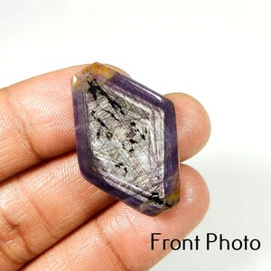 Può includere: Una gemma sfaccettata viola con una forma geometrica. La pietra ha un motivo interno argento e nero, con un tocco di giallo e marrone sui bordi. Il testo "Front Photo" è visibile.