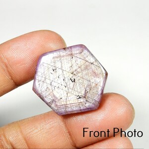 May include: A hexagonal, lavender gemstone with internal lines and inclusions. The stone is held between fingers, with the text "Front Photo" visible at the bottom.
