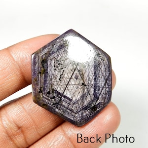 May include: A hexagonal, purple gemstone with a complex internal pattern of lines and inclusions. The stone has a polished surface and is held in a hand. The text "Back Photo" is visible at the bottom of the image.