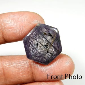 May include: A hexagonal, dark purple gemstone with a complex, web-like pattern of silver and black inclusions. The stone is held between fingers, with the text "Front Photo" visible at the bottom.
