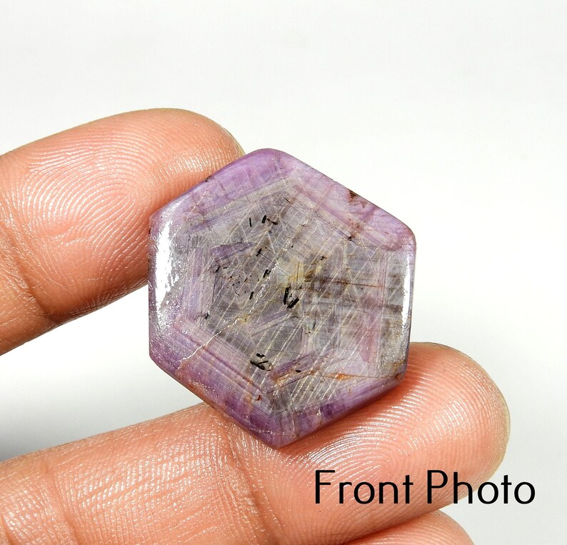 Op de afbeelding: Een zeshoekige, gepolijste edelsteen met een lichtpaarse tint. De steen is doorschijnend, met zichtbare interne lijnen en insluitsels. De tekst "Front Photo" is rechtsonder zichtbaar.