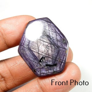Op de afbeelding: Een gefacetteerde, onregelmatig gevormde edelsteen met een diepe paarse tint, gekruist door fijne zwarte lijnen. De steen heeft een gepolijst oppervlak met een reflecterend gebied. De tekst "Front Photo" is zichtbaar aan de onderkant.