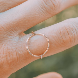 Könnte beinhalten: Ein einfacher goldener Ring mit einem Kreisdesign. Der Ring wird an einem Finger getragen.