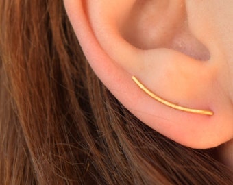 May include: A gold ear cuff earring with a curved bar design. The earring is worn in the upper cartilage of the ear.