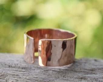 May include: A hammered copper ring with a split design. The ring is a warm copper color and has a rustic, handmade look.