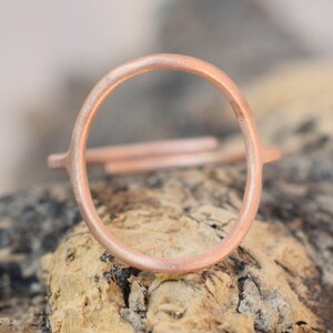 Peut inclure: Une bague en cuivre simple et minimaliste avec un design circulaire. La bague est présentée sur un morceau de bois usé.
