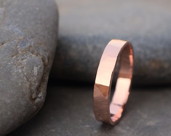May include: A hammered rose gold wedding band. The band is simple and elegant, with a smooth, polished finish.