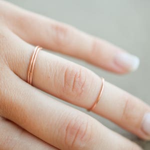 May include: A close-up of a hand wearing three thin, rose gold rings on the ring finger and one on the pinky finger.