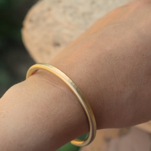 Op de afbeelding: Een gouden, gehamerd metalen armband. De armband is simpel en elegant, met een gladde, gepolijste afwerking.