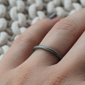 Puede incluir: Un anillo de banda de plata simple usado en un dedo.