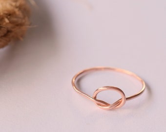 May include: A simple rose gold ring with a knot design.