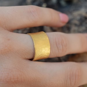 Peut inclure: Une large bague en or avec une texture martelée. La bague est portée sur un doigt.