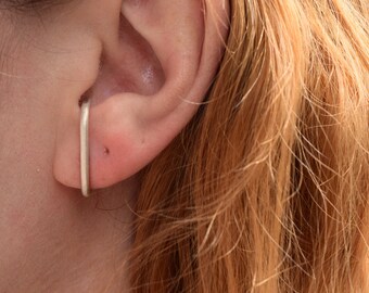 Può includere: Un orecchino a cerchio in argento con un designo semplice e dritto. Il cerchio viene indossato sulla parte superiore dell'orecchio, appena sopra il lobo.