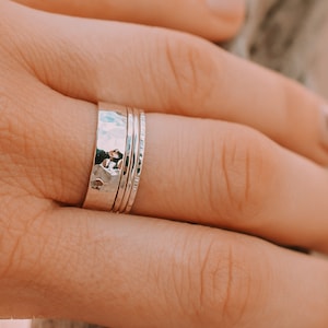 May include: A set of three silver rings, one with a hammered texture and two with a smooth finish. The rings are stacked on a finger.