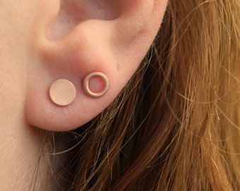 May include: A pair of gold-toned earrings, one is a solid circle and the other is a circle with a hollow center. The earrings are worn in the earlobe.