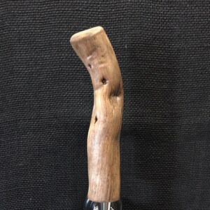 May include: A wooden tap handle with a natural, curved design. The handle is made of light brown wood and has a stainless steel base with a lever. The tap handle is designed for a kegerator or bar.