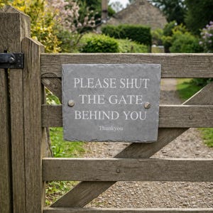 May include: A rectangular gray slate sign mounted on a wooden gate with two metal screws. The sign features white engraved text that reads: PLEASE SHUT THE GATE BEHIND YOU, followed by the word Thankyou centered at the bottom of the stone plaque.