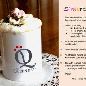 May include: A white mug with a gray "Q" logo and the text "The Queen Bean" is filled with a s'mores latte. The latte is topped with whipped cream, chocolate sauce, marshmallows, and graham cracker crumbs. The recipe for the s'mores latte is written on a pink background.