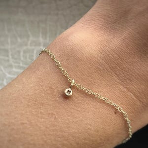 May include: A gold chain bracelet with a small charm featuring the letter "M".