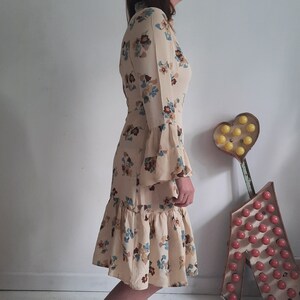 May include: A long-sleeved dress with a floral print in shades of brown, blue, and white. The dress has a high neckline and a ruffled skirt.