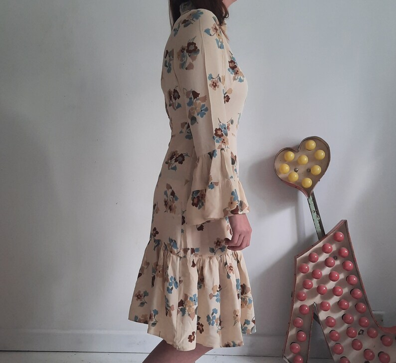May include: A long-sleeved dress with a floral print in shades of brown, blue, and white. The dress has a high neckline and a ruffled skirt.