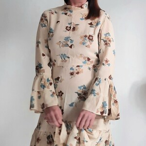 May include: A long-sleeved dress with a high neck and a floral print in shades of brown, blue, and white. The dress has a ruffled hem and bell sleeves.