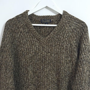 May include: A brown and white knitted jumper with a v-neck. The jumper has a label that says "P.G. Field" on it.