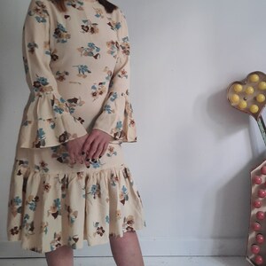 May include: A cream-colored dress with a floral print and bell sleeves. The dress has a tiered skirt and a fitted bodice.