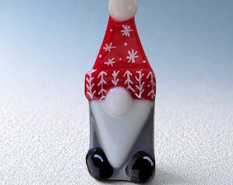 May include: A glass gnome figurine with a red hat decorated with white snowflakes and a white pom-pom. The gnome has a white beard, a gray body, and black shoes. The figurine is approximately 3 inches tall.