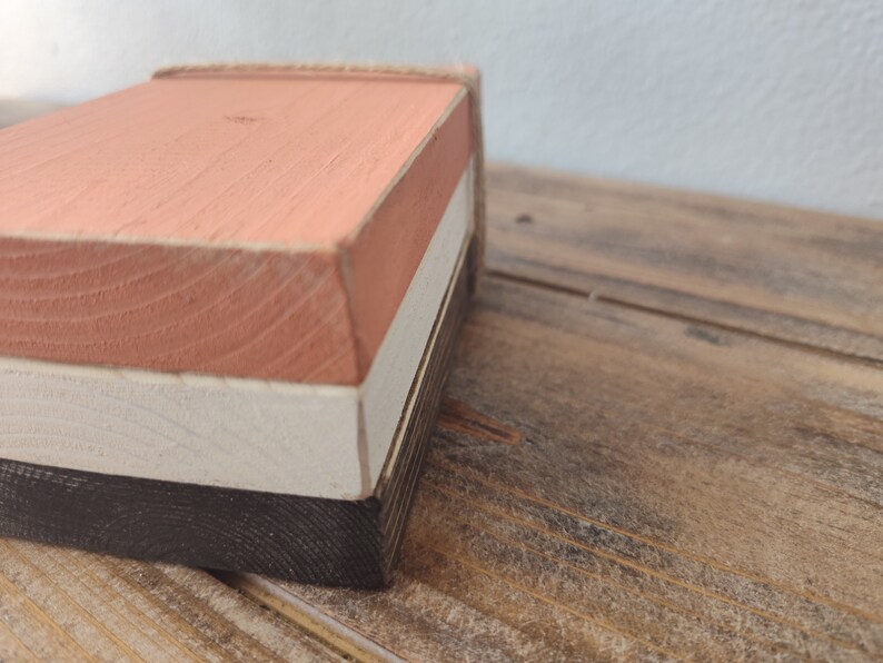 Puede incluir: Una caja de madera con tres capas pintadas en tonos rosa, blanco y negro. La caja est&aacute; hecha de madera natural y tiene un aspecto r&uacute;stico.