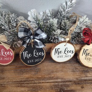 May include: Four round wood slice ornaments with the text "The Lees EST. 2023" on each. Two ornaments are painted black, one is white, and one is red.