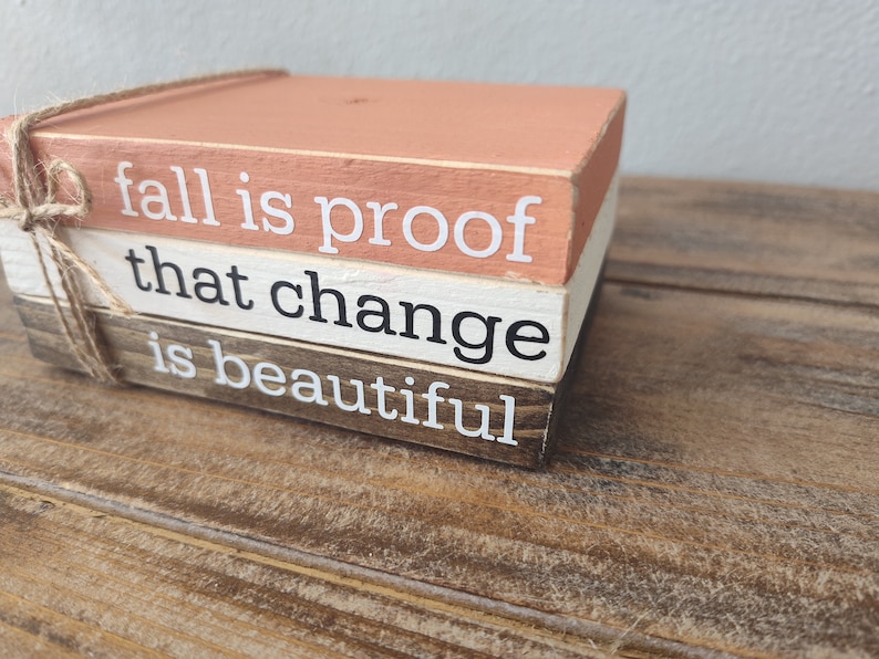 Puede incluir: Una pila de tres bloques de madera con una cita sobre el oto&ntilde;o: "fall is proof that change is beautiful". Los bloques est&aacute;n pintados en tonos de marr&oacute;n, blanco y melocot&oacute;n.