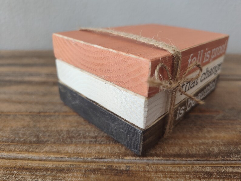 Puede incluir: Tres bloques de madera apilados uno encima del otro, atados con un cordel. El bloque superior est&aacute; pintado de color naranja claro y tiene el texto "fall is proof that change is beautiful" escrito en &eacute;l.