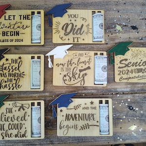 May include: Six wooden graduation cards with a slot for a rolled-up bill of money. Each card features a different graduation-themed message and a graduation cap. The messages include "Let the adventure begin", "You did it", "The tassel was worth the hassle", "And now the limit is the sky", "She believed she could so she did", and "And the adventure begins".