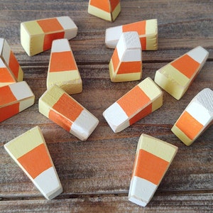 May include: A collection of 11 wooden candy corn decorations painted in yellow, orange, and white. The candy corn is arranged on a wooden surface.