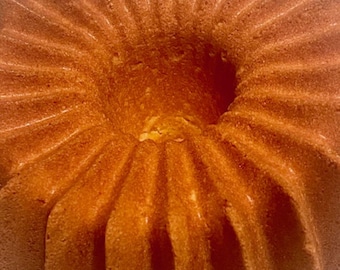 May include: A golden-brown bundt cake with a fluted design, resting on a wire rack. The cake has a central hole and a textured surface, showcasing its baked form. The cake's color suggests a rich, buttery flavor.