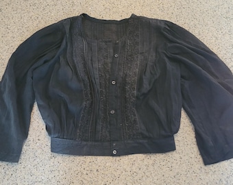 May include: A dark gray blouse with long, flared sleeves and a button-down front. The blouse features detailed embroidery and pleating down the center. The fabric appears to be lightweight and slightly textured, with a subtle sheen.