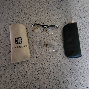 Puede incluir: Dos pares de gafas con monturas negras y plateadas y lentes transparentes. Un par está en una funda negra y el otro en una funda beige con el logotipo de Givenchy.