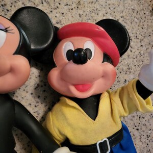 May include: A vintage Mickey Mouse and Minnie Mouse plush toy set. Mickey is wearing a red hat, yellow shirt, blue pants, and a black belt. Minnie is wearing a black dress and has a red bow on her head.
