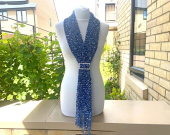 May include: A blue beaded scarf with a silver clasp. The scarf is displayed on a white mannequin.