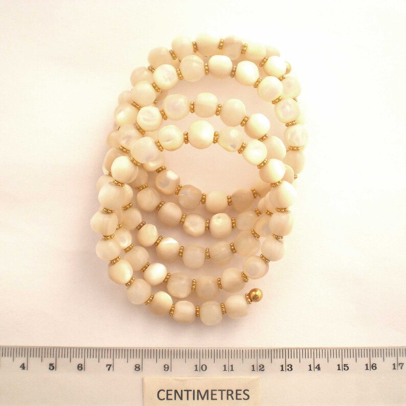 This unique handmade memory wire bracelet has more than 90 white mother of pearl beads interspersed with tiny gold plated spacer beads.  It is finished with gold plated end caps. It will fit any size of wrist, with four to five circles in total.