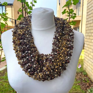 May include: A multi-toned, hand-knitted infinity scarf in shades of brown, gold, and silver. The looped scarf is displayed on a white mannequin, highlighting its textured design. This accessory is ideal for adding warmth and style to any outfit.
