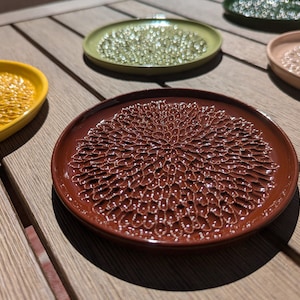 Peut inclure: Quatre sous-verres en céramique avec un motif texturé en forme de fleur. Les sous-verres sont dans des tons de jaune, vert, marron et rose.