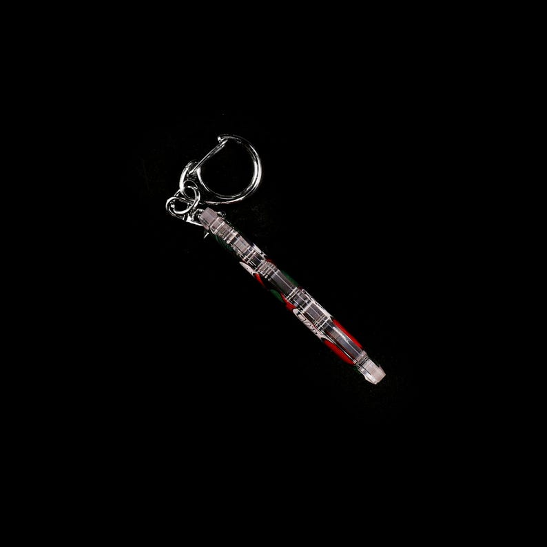 May include: A clear, rectangular keychain with a silver metal ring. The keychain has a pattern of red, green, and silver stripes. The background is solid black.