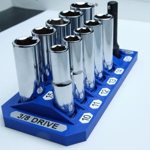 May include: A set of chrome sockets in a blue holder. The sockets are arranged in a row and are of varying sizes, with the numbers 10 through 15 and 5/8 inch, 1/2 inch, 9/16 inch, and 14 clearly visible. The holder is labeled "3/8 DRIVE."